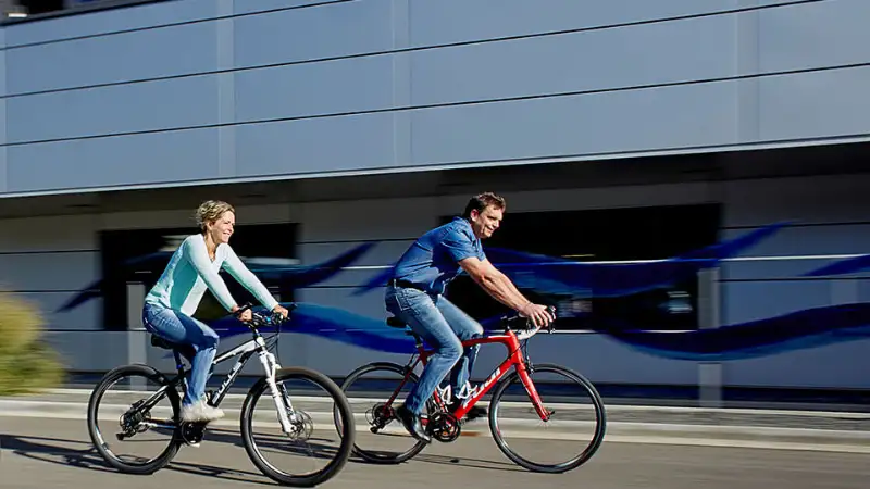 Zwei Menschen, die auf zwei Stadträdern vor einem Büro-Gebäude vorbeifahren