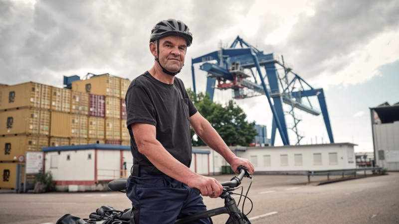JobRadler steht am Containerhafen und blickt selbstbewusst in die Kamera JobRadler steht am Containerhafen und blickt selbstbewusst in die Kamera