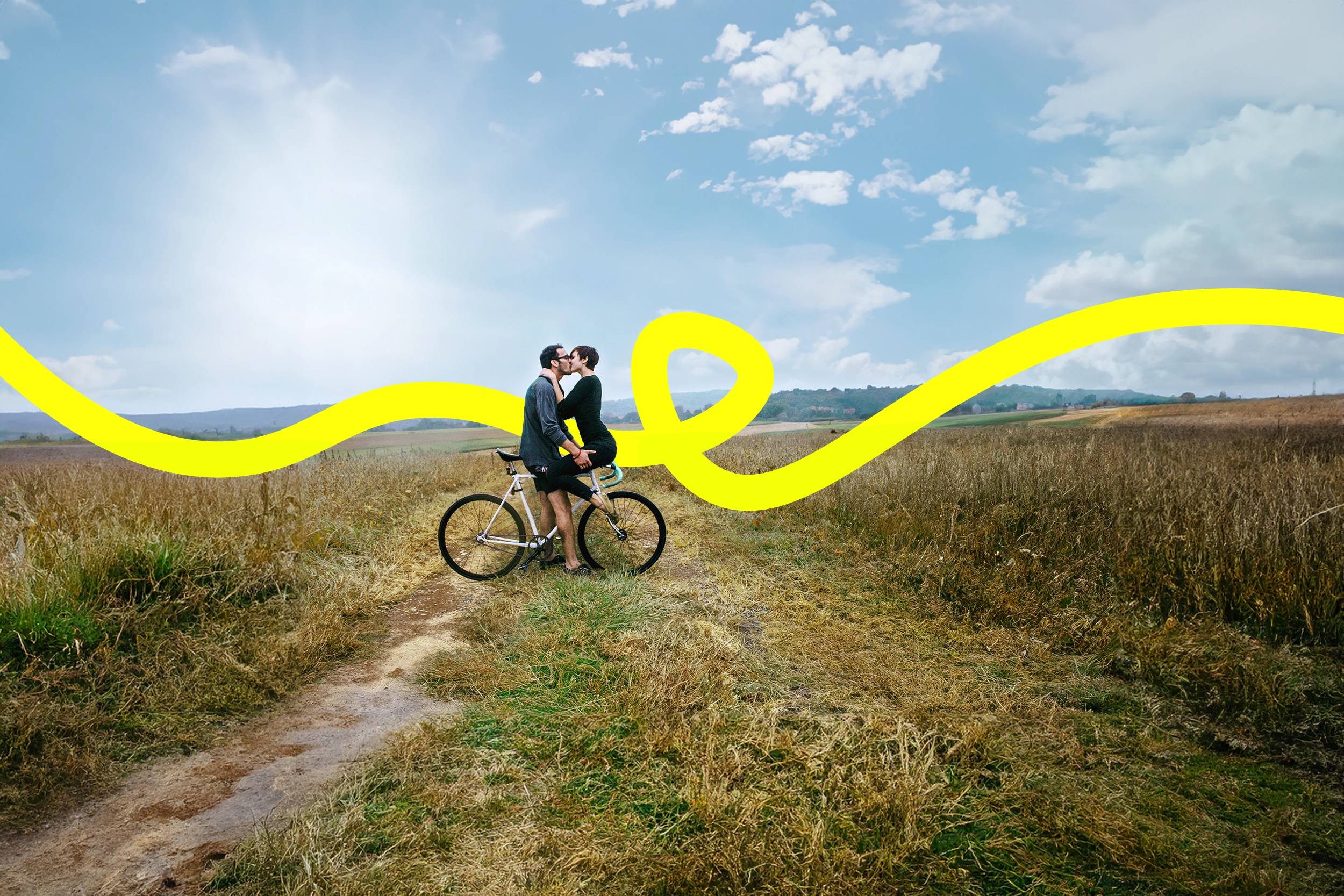 Ein Heteropärchen küsst auf dem Fahrrad auf dem Feldweg, die JobRad Loop Linie kringelt sich durchs Bild Ein Heteropärchen küsst auf dem Fahrrad auf dem Feldweg, die JobRad Loop Linie kringelt sich durchs Bild