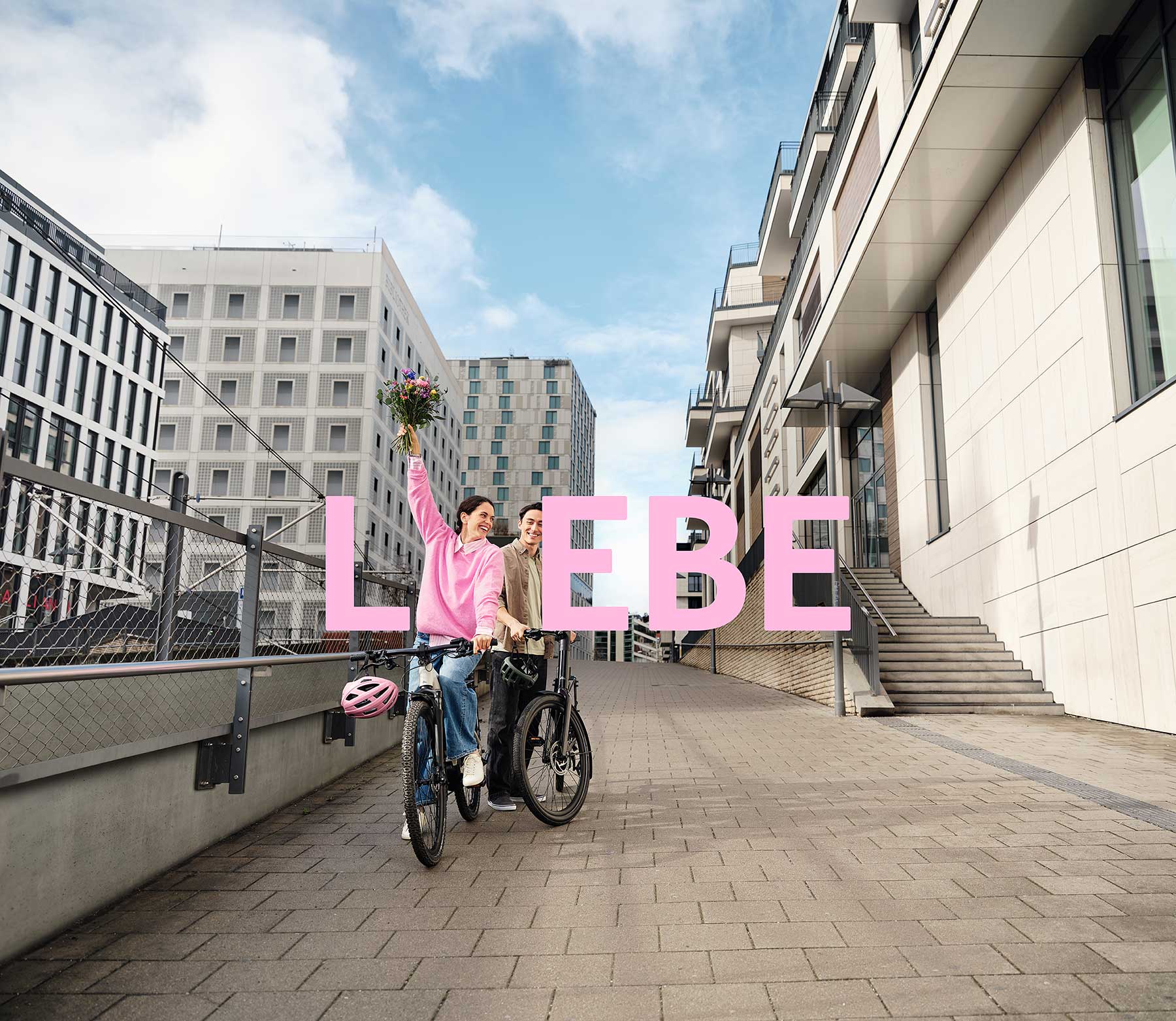 2 JobRadler:innen auf einem Fahrrad in einem urbanen Umfeld mit einem Blumenstrauß.